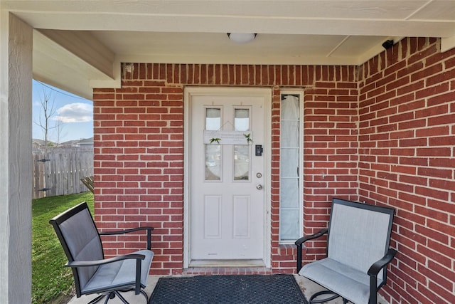 doorway to property featuring brick siding and fence