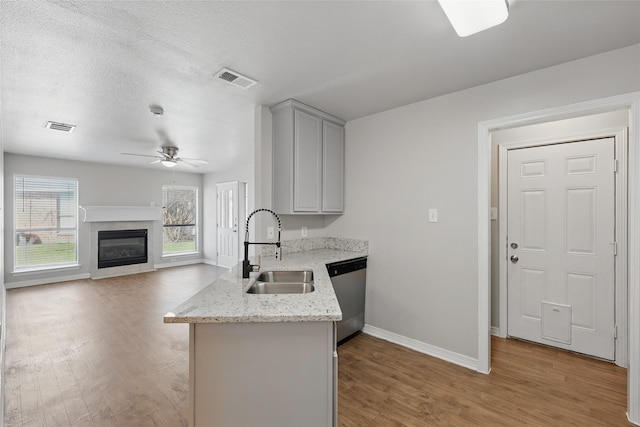 kitchen featuring light wood finished floors, visible vents, gray cabinetry, stainless steel dishwasher, and a sink