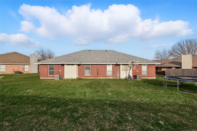 back of house with brick siding, a lawn, central AC, and a trampoline