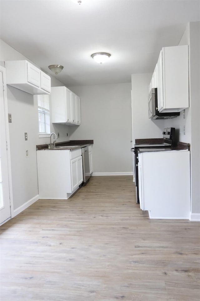 kitchen with dark countertops, white cabinetry, light wood-style floors, appliances with stainless steel finishes, and baseboards