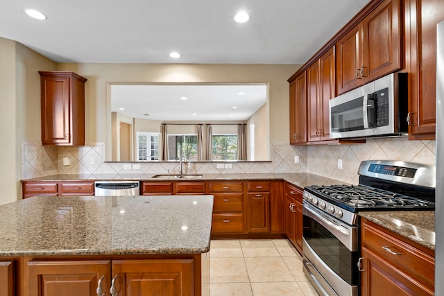 kitchen with a sink, light stone countertops, appliances with stainless steel finishes, and brown cabinets