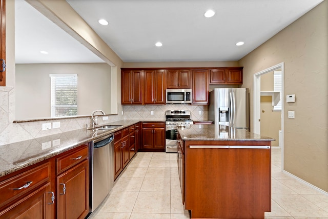 kitchen with a center island, stone counters, appliances with stainless steel finishes, light tile patterned flooring, and a sink