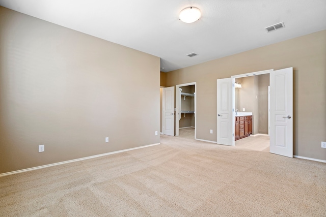 unfurnished bedroom with a spacious closet, baseboards, visible vents, and light carpet