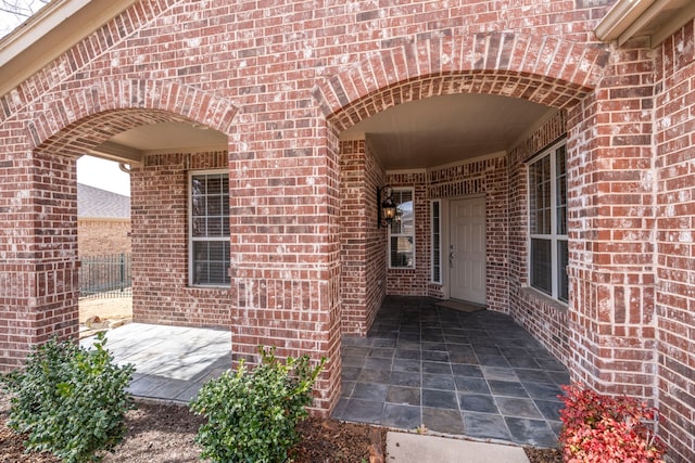 view of exterior entry with brick siding and fence