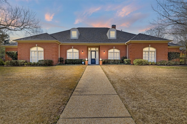 view of front of home with brick siding, a chimney, a front lawn, and a shingled roof