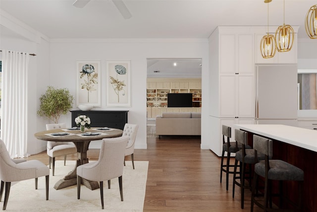 dining area featuring built in features, wood finished floors, ornamental molding, and ceiling fan with notable chandelier