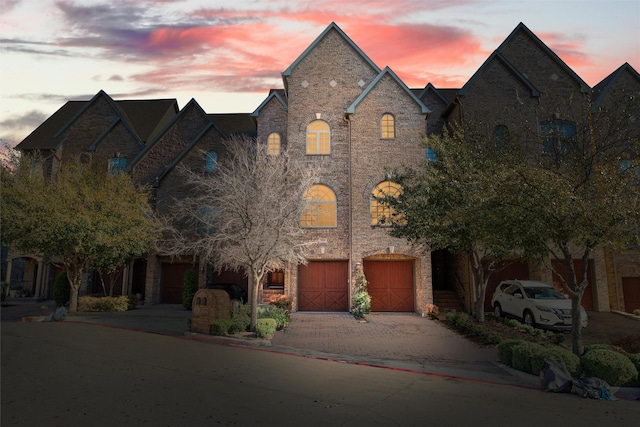 french country home featuring decorative driveway, a garage, and brick siding