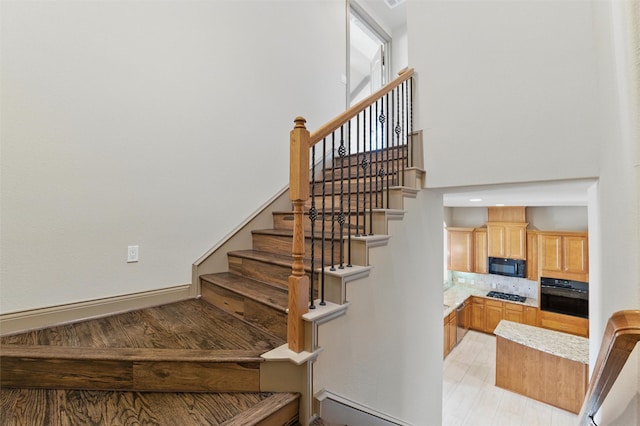 staircase with wood finished floors, baseboards, and a towering ceiling