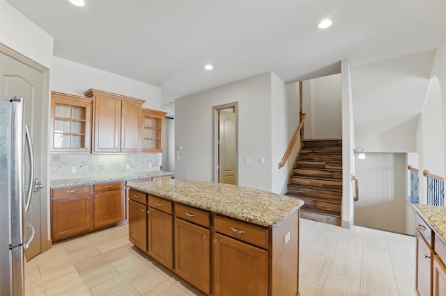 kitchen featuring a center island, light stone counters, decorative backsplash, brown cabinets, and freestanding refrigerator