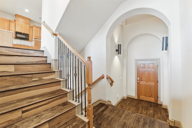 foyer entrance with baseboards, recessed lighting, arched walkways, a towering ceiling, and dark wood-style floors