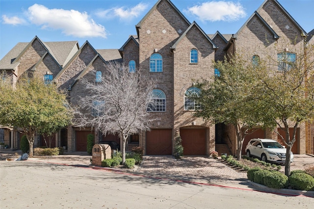 french country style house with decorative driveway, brick siding, and an attached garage