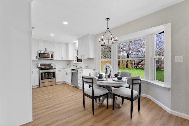 kitchen with an inviting chandelier, light countertops, white cabinets, appliances with stainless steel finishes, and light wood-type flooring