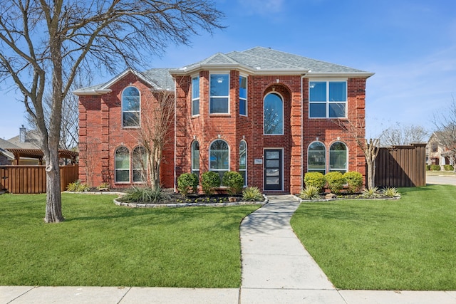 view of front of house featuring brick siding, roof with shingles, a front yard, and fence