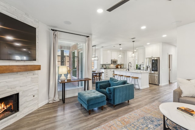 living area featuring baseboards, a stone fireplace, recessed lighting, light wood-style flooring, and a ceiling fan