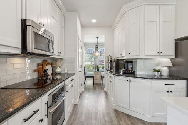 kitchen with light wood-type flooring, appliances with stainless steel finishes, white cabinetry, tasteful backsplash, and a chandelier