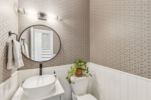 bathroom with wainscoting, wallpapered walls, toilet, and a sink