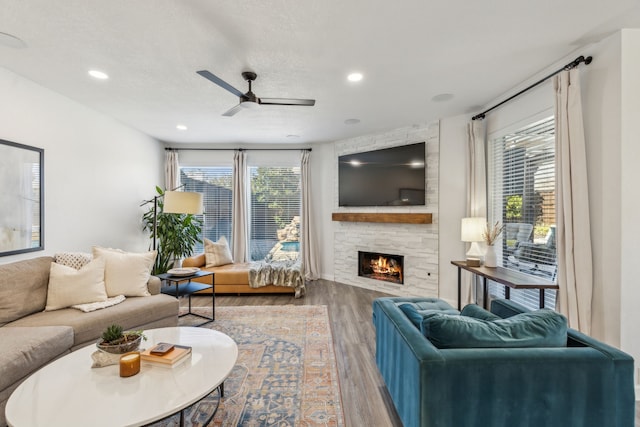 living area featuring a ceiling fan, a textured ceiling, wood finished floors, recessed lighting, and a fireplace