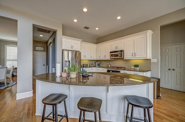 kitchen featuring visible vents, white cabinets, appliances with stainless steel finishes, a kitchen breakfast bar, and backsplash