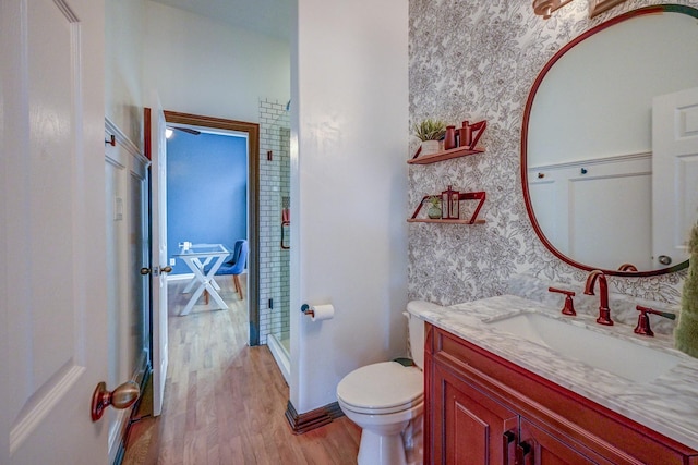 bathroom with toilet, wood finished floors, vanity, and wallpapered walls