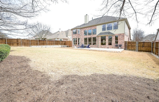 rear view of house with brick siding, a fenced backyard, a chimney, and a patio area