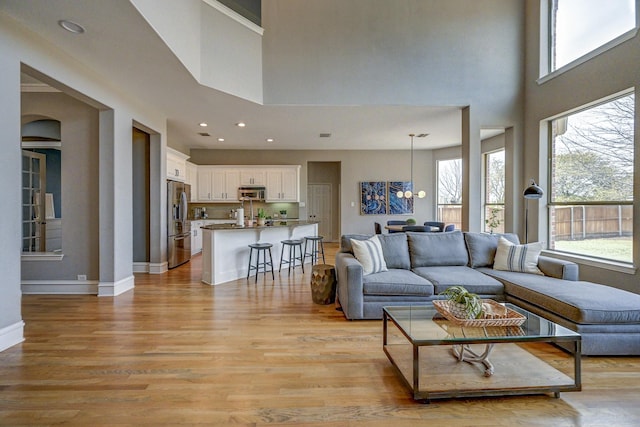 living room with recessed lighting, a high ceiling, light wood-type flooring, and baseboards