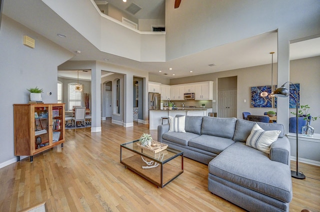 living area with light wood-type flooring, visible vents, arched walkways, baseboards, and a towering ceiling