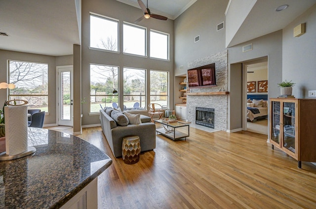 living room featuring light wood finished floors, visible vents, a fireplace, and ceiling fan