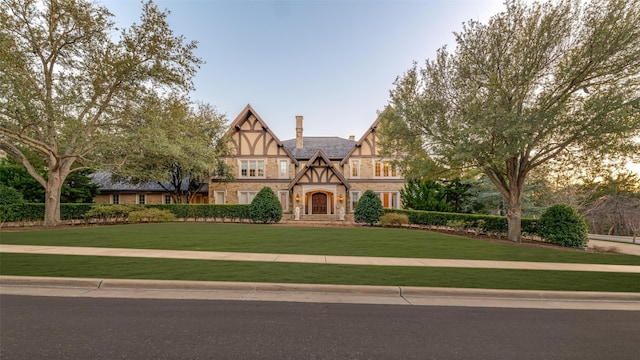 tudor home featuring a front yard, stucco siding, stone siding, and a chimney