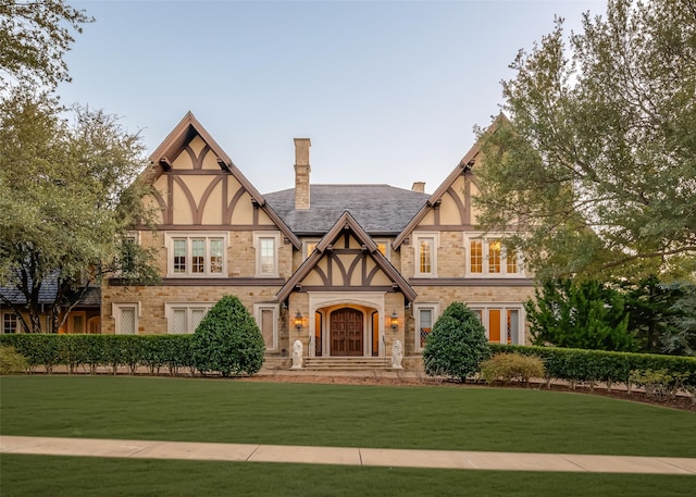 tudor home featuring stucco siding, a chimney, and a front yard