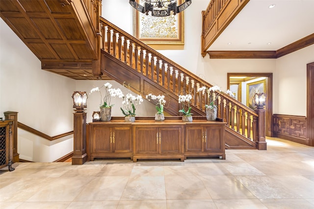 stairway featuring an inviting chandelier, ornamental molding, a towering ceiling, and wainscoting