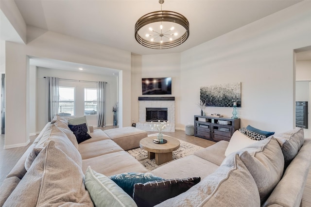 living room with a stone fireplace, an inviting chandelier, wood finished floors, and baseboards