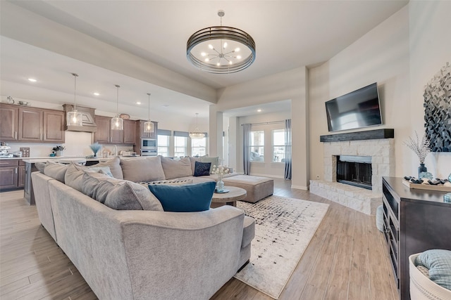 living area featuring a stone fireplace, an inviting chandelier, and light wood finished floors