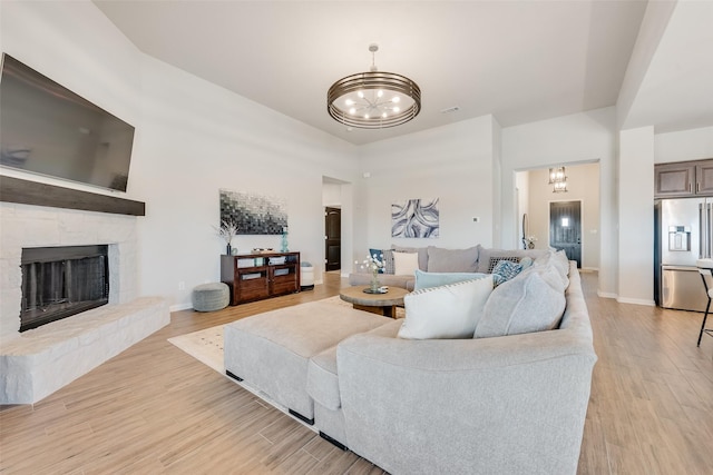 living room featuring a chandelier, a fireplace, light wood-type flooring, and baseboards