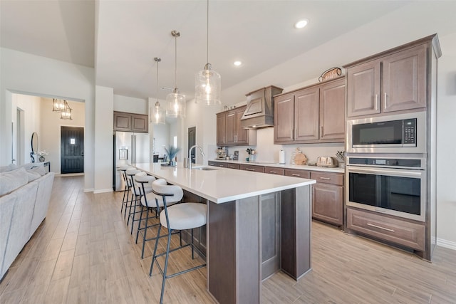 kitchen with premium range hood, light wood-style flooring, a sink, a kitchen breakfast bar, and stainless steel appliances