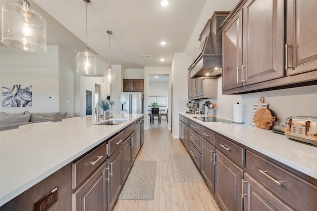 kitchen featuring light wood finished floors, custom exhaust hood, stainless steel appliances, a sink, and light countertops