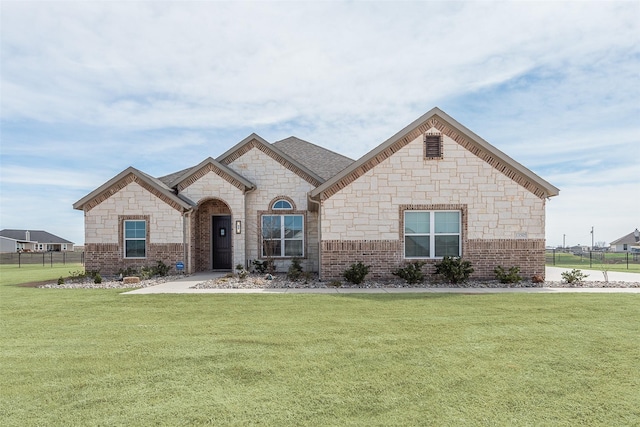 french country inspired facade with brick siding, a front yard, fence, and stone siding