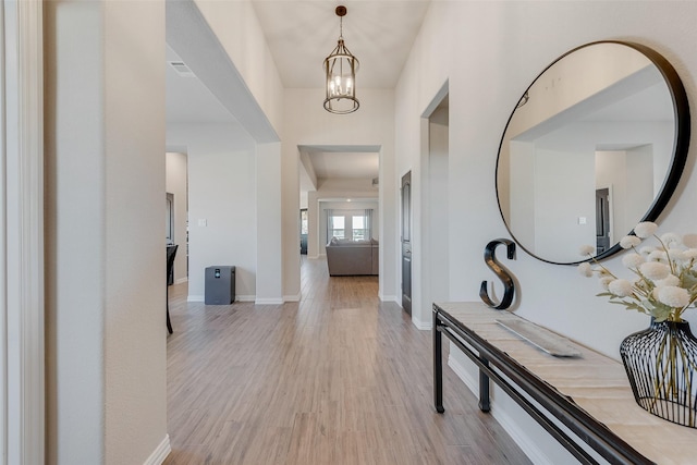 hallway featuring light wood finished floors, a notable chandelier, visible vents, and baseboards