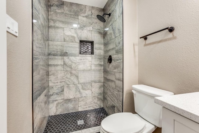 bathroom with tiled shower, toilet, vanity, and a textured wall