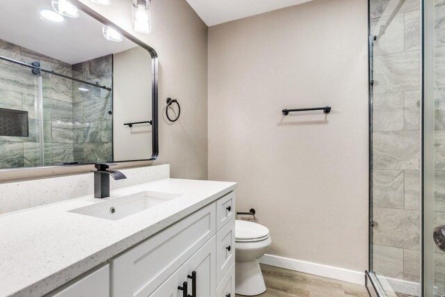 full bath featuring baseboards, toilet, wood finished floors, and a shower stall