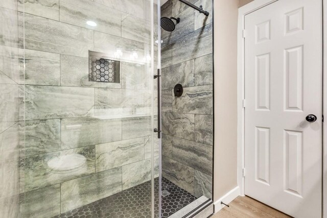 full bath featuring a shower stall, baseboards, and wood finished floors