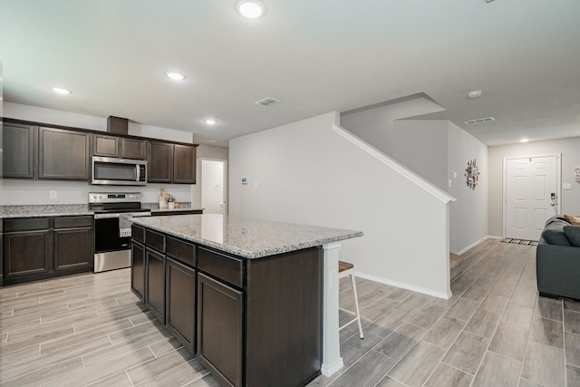 kitchen with wood tiled floor, stainless steel appliances, dark brown cabinets, a kitchen breakfast bar, and a center island