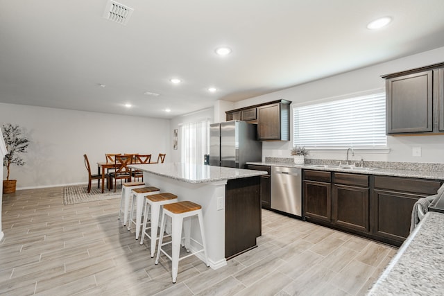 kitchen featuring a sink, a kitchen island, dark brown cabinetry, appliances with stainless steel finishes, and a breakfast bar area