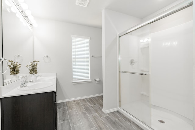 full bathroom with visible vents, wood finish floors, double vanity, a stall shower, and a sink