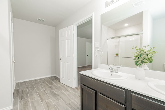 bathroom with double vanity, a shower with shower door, visible vents, and a sink