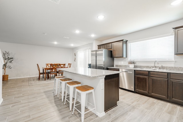 kitchen featuring a kitchen island, light stone counters, a kitchen breakfast bar, stainless steel appliances, and a sink