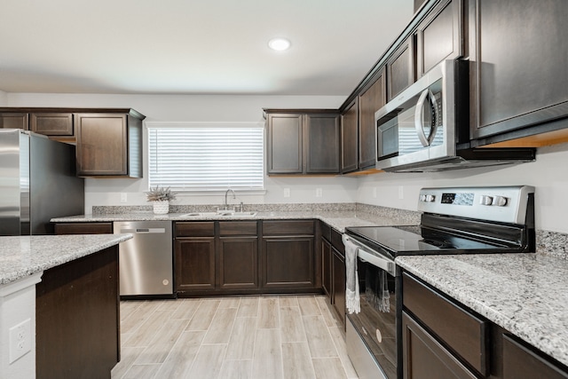 kitchen featuring light wood finished floors, dark brown cabinets, light stone countertops, appliances with stainless steel finishes, and a sink