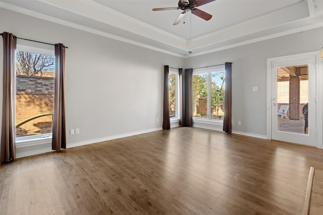 spare room with a tray ceiling, wood finished floors, crown molding, baseboards, and ceiling fan