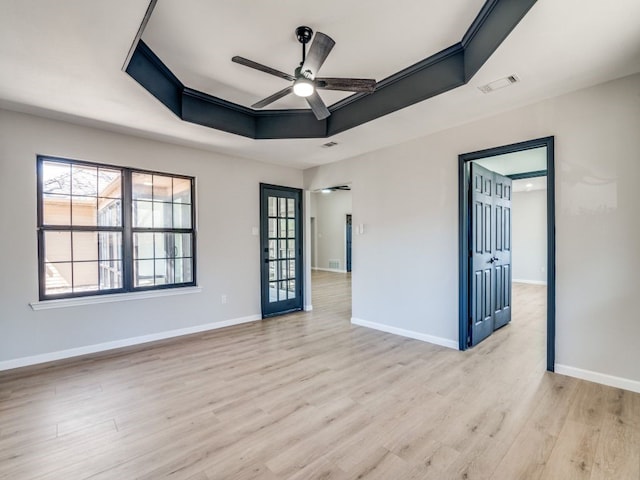 unfurnished room with a raised ceiling, light wood-style flooring, visible vents, and a wealth of natural light