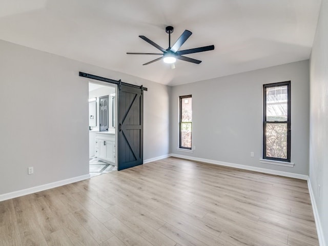 spare room with a barn door, baseboards, light wood finished floors, and ceiling fan