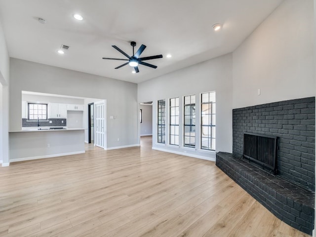 unfurnished living room featuring baseboards, visible vents, ceiling fan, light wood-style floors, and a brick fireplace